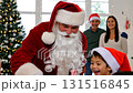 Santa Claus giving candy canes to excited Asian children during Christmas family celebration at home with decorated tree 131516845