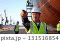 European construction manager shouting and pointing angrily at shipyard workers near large vessel hull with safety equipment 131516854