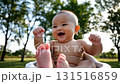 Adorable Asian baby laughing and waving hands joyfully outdoors in natural park setting with green trees background 131516859