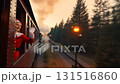 Young caucasian woman in santa costume waving from vintage steam train window traveling through forest at golden hour sunset during christmas season 131516860