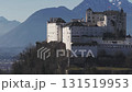 Aerial view of Hohensalzburg Fortress in Salzburg, Austria, with medieval architecture, winter trees, and snow capped mountains in the background. 131519953