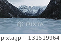 A serene frozen lake in the Dolomites, Italy, with snow covered peaks and dark forested slopes. The camera moves slowly forward, revealing the landscape. 131519964