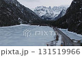 A serene frozen lake with textured ice, surrounded by snow covered peaks and dense evergreen forests in the Dolomites, Italy. Smooth camera motion. 131519966