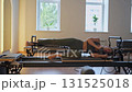 Tired and happy woman practices Pilates on reformer equipment, showcasing her flexibility and strength dynamically 131525018