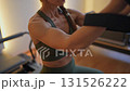 Woman doing pilates exercise on Pilates Reformer for the chest, arms biceps and back muscles, focusing on flexibility, strength, and control with determination 131526222
