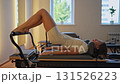 Woman training on the reformer bed at Glute bridge Pilates workout. Reformer pilates studio machine for fitness workouts in gym. Fit, healthy and strong authentical body. Fitness concept 131526223