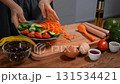 Woman preparing breakfast. Chopping vegetables, cucumber, carrot, tomato, avocado on board. 131534421