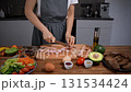 Woman slicing sausage on cutting board. Breakfast ingredients around. Close-up. 131534424