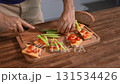 Unrecognizable man preparing a tasty snack. Bruschetta with cheese and vegetables. 131534426