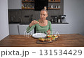 Woman eating bruschetta with cheese and vegetables in her kitchen. Tasty snack. 131534429