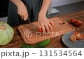Woman cutting red bell pepper on a wooden board. Close-up, kitchen prep. 131534564
