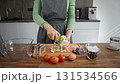 Female hands preparing vegetable breakfast, peeling zucchini. Tomatoes, olives, basil on table. 131534566