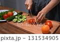 Woman chopping vegetables for salad, cucumbers and tomatoes. Close-up, fresh ingredients. 131534905