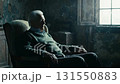 An elderly man sits near the window of an old house all alone. 131550883