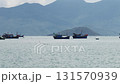 Beautiful tranquil seascape with traditional vietnamese fishing boats floating on the calm water of a bay, with a hazy mountain range silhouetted in the background on an overcast day 131570939