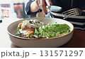 Close up of a woman's hands cutting an avocado toast with poached egg and salmon with a knife and fork at a restaurant. Delicious and healthy breakfast idea with fresh ingredients for a balanced diet 131571297
