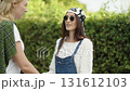 Fashionable friends engage in lively conversation outdoors with bright greenery in the background on a sunny day 131612103