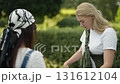 Two friends chat and enjoy a sunny day outside in a beautiful garden setting 131612104
