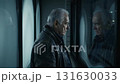 An elderly man stands alone at the window of an old house. 131630033
