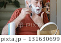 Senior Man shaving his face. Old male shaves beard and mustache with shaver. Elderly gray haired man looking at the mirror, applies shaving cream foam and using razor. Skin hygiene. Daily body care 131630699