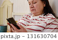 Senior woman having breakfast sitting in bed, drinking tea, enjoying her morning at home. Old lady eating from tray and using phone. Elderly female in pajamas relaxing with cup of coffee in a bedroom. 131630704