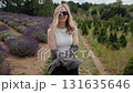 Portrait of cheerful blonde woman wearing sunglasses and checkered shirt over white top, posing and enjoying herself in beautiful lavender field. Blonde woman walking amid blooming lavender field 131635646