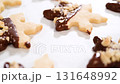 Creating cutout sugar cookies, partially dipped in chocolate and topped with hazelnut pieces, placed on parchment paper. 131648992