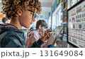 A curly haired student leans toward his tablet with serious focus, the large classroom display glowing nearby. The moment captures concentration in digital learning. 131649084