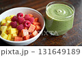 Healthy green smoothie and fresh fruit bowl with mango, papaya, and raspberries on wood 131649189