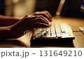 Close up of hands typing on a computer keyboard in a dimly lit office at night 131649210