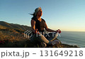 Peaceful woman meditating on a mountain cliff with ocean view during sunset 131649218