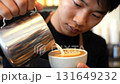 Skilled asian barista pouring steamed milk into a coffee cup, creating intricate latte art 131649232