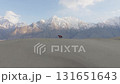 Aerial view of a majestic desert landscape in Pakistan, featuring snow-capped mountains and a lone rider on horseback 131651643