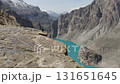 Aerial view of a breathtaking mountain valley in Pakistan, featuring a stunning turquoise lake, rugged peaks and a woman atop the cliff 131651645