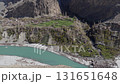 Aerial view of a serene village nestled in the mountains of Pakistan, showcasing lush terraced fields and a tranquil turquoise river 131651648