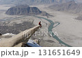 Aerial view of a man perched on a rock pinnacle overlooking a river in the mountains of Pakistan 131651649