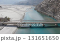 Aerial view of a turquoise river flowing through a snowy landscape in Pakistan, highlighting a solitary motorcycle crossing a bridge 131651650