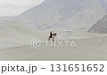 Aerial view of a solitary horseback rider traversing the vast sand dunes of Pakistan's mountainous region 131651652