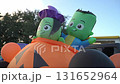 A pair of green inflatable characters ride on a large orange pumpkin decoration at a school parking-lot event. Festive balloons and evening sky set a playful holiday mood. 131652964