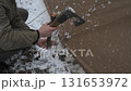 A person is securing a tent stake into the snowy ground using a axe 131653972