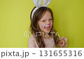 A funny laughing girl with a painted face in the guise of a rabbit with white ears dances merrily. The feast of Holy Easter. 131655316