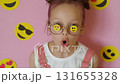 A beautiful stylish sweet girl looks through glasses with emoji stickers, blowing a kiss. A way to convey emotions through emoticons 131655328