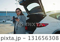 Woman is using her smartphone while standing by a car during the winter season 131656308