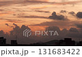 A vibrant sunset with orange and purple hues over a city skyline. Silhouettes of buildings and clouds create a dramatic scene. 131683422