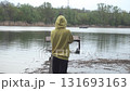 a young girl in a stylish hoodie walks along a wooden bridge for fishing, a motorboat is going in the background, the wind is blowing, on the other bank there is a thicket of green trees 131693163