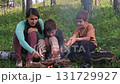 Family camping and cooking sausages on sticks over campfire 131729927