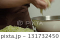 View back on the peel the zucchini. 4K close-up: A chef transfers sliced zucchini, but first squeezes the juice out of the zucchini and places it in a metal bowl on a wooden plate set on a rustic 131732450