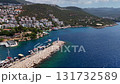 Aerial view of Kas harbor and lighthouse in Turkey, showing turquoise sea, boats, and hillside houses surrounded by lush greenery and coastal mountains. 131732589