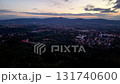 A beautiful aerial view of a vibrant city at twilight, surrounded by lush vegetation and distant mountains 131740600