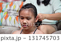 A warm and candid moment of a mother braiding her daughter's hair while the little girl smiles brightly at home. 131745703